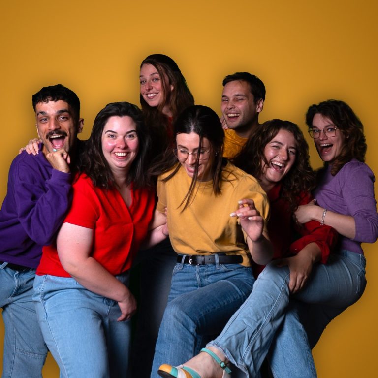Groepsfoto CHAOS Groep van zeven mensen die vrolijk poseren voor een gele achtergrond.